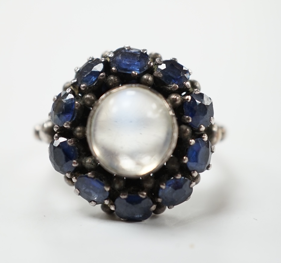 An Arts & Crafts white metal, moonstone and sapphire set circular cluster ring, in the manner of Sibyl Dunlop, size M. Condition - fair